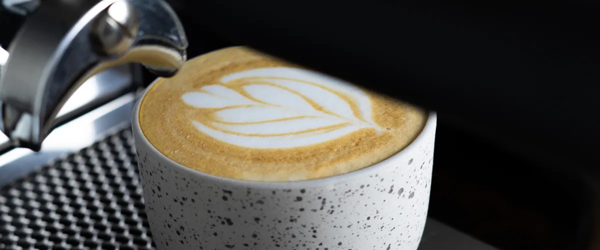 Kopje koffie met latte art onder de espressomachine